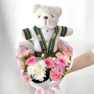 White teddy bear in a Chula graduation gown surrounded by pink and white flowers.