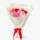 Crocheted pink and red hearts in a bouquet wrapped in white paper and tied with a red ribbon.