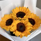 Bouquet of four bright yellow sunflowers with dark centers, wrapped in white paper.