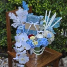 Blue Songkran gift set with blue scarf, white orchids, hydrangeas, and decorative elements in a silver bucket.