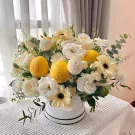 White flowers and lemons arranged in a white box with a black trim.