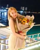 Woman holding a sunflower bouquet on a balcony at night with city lights in the background.