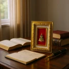 Gold-framed Emerald Buddha with green crystals sits on a wooden desk next to books and a pen.
