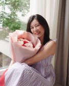 A young woman with dark hair smiles holding a pink bouquet of carnations.