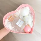 Heart-shaped pink gift box with a teddy bear towel, rose bath salts, bath bomb, and wooden spoon.
