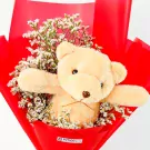 Teddy bear peeking from a bouquet of white flowers in red wrapping.