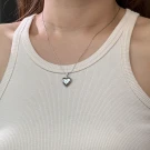 Silver heart locket necklace on a woman's chest, resting on a white ribbed tank top.