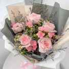Pink roses, carnations, daisies, and caspia flowers in a bouquet with light pink ribbon.