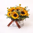 White box overflowing with sunflowers and small white flowers, tied with a brown ribbon.