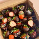 Box of chocolate-dipped strawberries with sprinkles and some sliced in half.