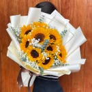 A bouquet of ten golden sunflowers with baby's breath and eucalyptus, wrapped in white paper.