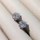 Two round-cut moissanite diamond solitaire earrings on a textured surface.