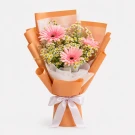 Pink gerberas and white daisies in an orange wrapper, tied with a white ribbon.