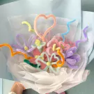 Bouquet of colorful pipe cleaner flowers, including a heart shape, on a light blue background.