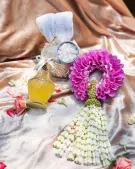 Thai Water Ceremony Set with jasmine garland, pink flower, yellow bottle, and rolled white towels.