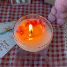 Lit Valentine's candle in coupe glass with orange wax, pink flowers, and a hidden message.