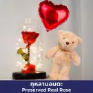 A preserved red rose under a glass dome with fairy lights, a teddy bear, and a red heart balloon.