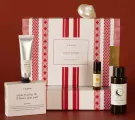 Yahn premium gift set with hand cream, soap bar, perfume roller, and body oil on red background.