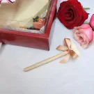 White chocolate heart cake pop with a bow on a wooden stick, next to a red box and roses.