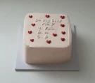 Square pink cake with red hearts and "Do you love me?" message.