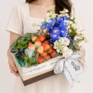 Fruit and flower gift box with strawberries, grapes, blue and white flowers, and a ribbon.