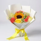 A bouquet of a sunflower, yellow rose, pink carnations, and baby's breath, wrapped in white paper and tied with a yellow ribbon.