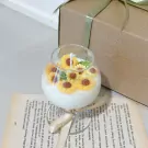 Sunflower scented candle in a wine glass with tiny sunflower decorations, next to a gift box and open book.
