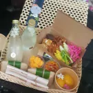 Khao Chae set with rice, bottles of jasmine water, mangoes, and various savory side dishes in a woven basket.