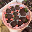 Chocolate-covered strawberries with pink candy accents in a round pink box.