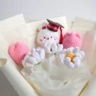 Crocheted graduation bouquet with white flowers, pink tulips, and a stuffed animal wearing a cap.