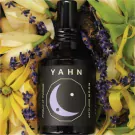 Bottle of Yahn Moon Deep Sleep pillow mist surrounded by lavender and yellow flowers.