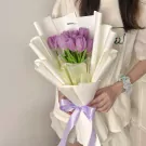 A bouquet of purple tulips wrapped in white paper with a purple ribbon.