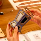 Hands assembling a blue and gold wooden carousel model, holding a circular wooden piece.