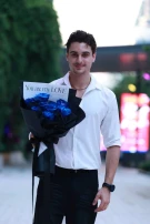 Man holding a bouquet of blue roses in black wrapping with a card that says "You are my LOVE".