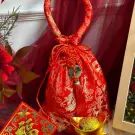 Red Chinese New Year pouch with golden dragon pattern, tassels, and jade charm.