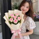 Bouquet of six pink roses, wrapped in white paper, tied with a pink ribbon.