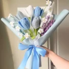 Crocheted bouquet of blue, grey, and white tulips with purple accents, wrapped in blue paper and tied with a blue ribbon.