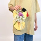 A person holds a yellow graduation card with a rose and baby's breath, topped with a mini graduation cap.
