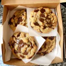Box of four large, golden brown chocolate chip cookies, with gooey, melted chocolate chunks.