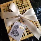 A woven box tied with a cream ribbon, holding fresh flowers and a tag with roses.