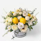 White floral arrangement with lemons in a round box.
