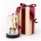 Glass dome with holographic rose, kissing couple figurine, and fairy lights next to a wrapped gift box.