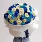 Large bouquet of blue, turquoise, and white roses wrapped in white paper with a dark blue ribbon.