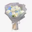 Bouquet of white roses and blue hydrangeas with daisies, wrapped in gray paper and tied with a white ribbon.