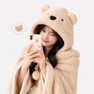 Young person wearing a fluffy, teddy bear-themed hoodie blanket, holding a phone.