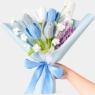Crocheted bouquet of blue, grey, and white tulips with purple accents, wrapped in blue paper and tied with a blue ribbon.