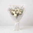 Bouquet of twelve white roses with dried filler flowers, wrapped in white paper and tied with a white ribbon.