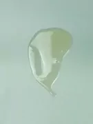 A viscous, translucent light green liquid dollop with air bubbles against a muted light blue background.