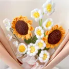 Crocheted sunflower bouquet with white flowers, green leaves, and pink wrapping.