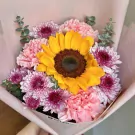 Bouquet of a large sunflower surrounded by pink carnations and purple-pink chrysanthemums.